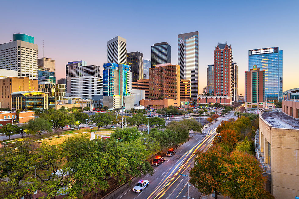 Houston city skyline during sunset with tall modern buildings and trees lining the street below.