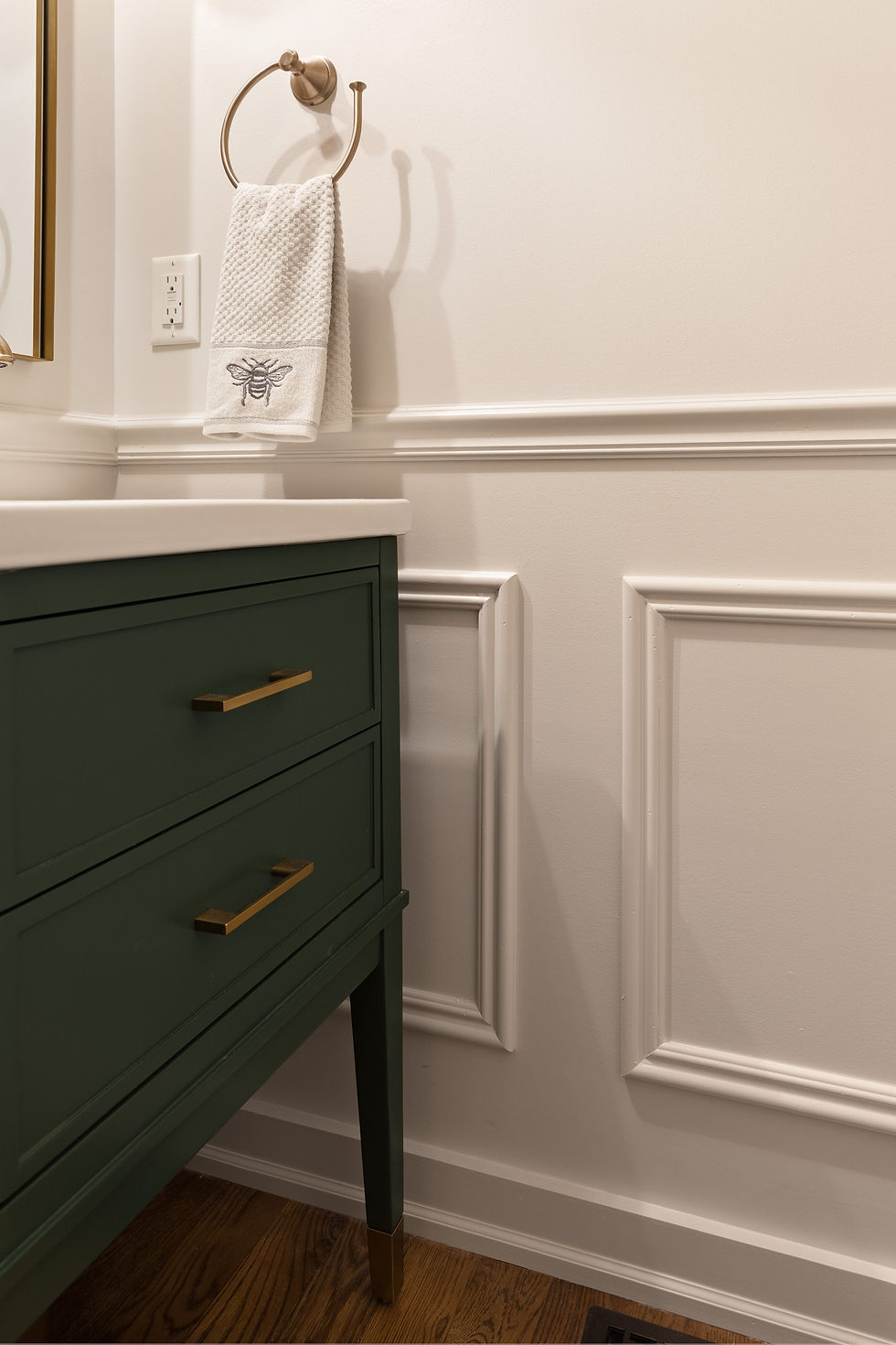 A creamy powder room with decorative trim and a green vanity.