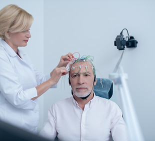 EEG examination. Female neurologist adjusting electrodes on gray-haired male patient head
