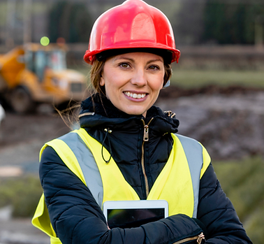 A talented mum in construction leadership. She is on site wearing a hi vis vest and red hard hat. She is smiling because her organisation supports talented mums to stay in construction and to progress into leadership roles.
