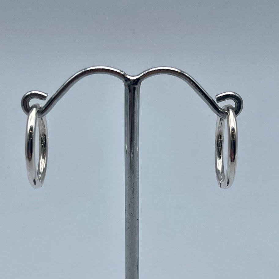Round Huggie Earrings hanging on a black stand, showing the close-fitting silver hoop design.