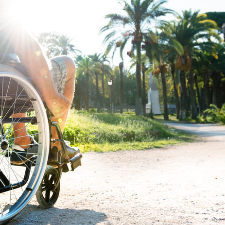 person in wheelchair rolling on outside trail on a sunny day