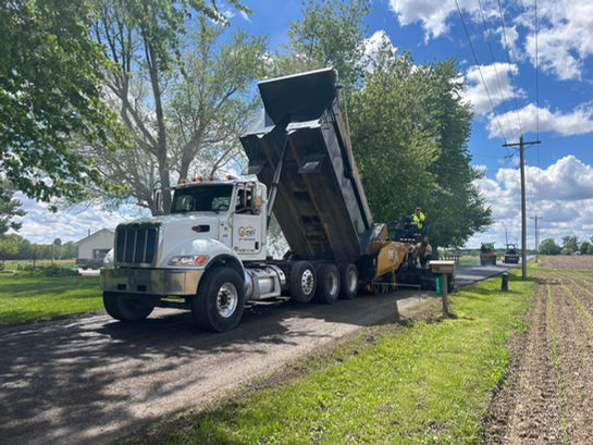 Dump truck feeding asphalt into paver during road paving operation