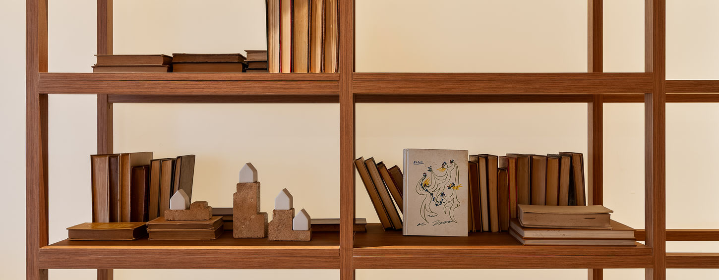 Detalhe de estante divisória vazada em marcenaria de madeira natural com iluminação embutida (backlight). O móvel planejado expõe livros e objetos de decoração com simetria e elegância. Projeto executado pela marcenaria boutique TRACIATTO para a CASACOR Brasília, traduzindo estética atemporal e precisão construtiva de alto padrão.