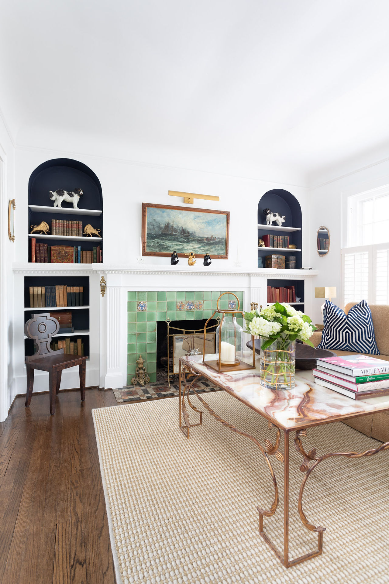 Living room with arched navy built-in bookshelves, green tile fireplace, and marble coffee table