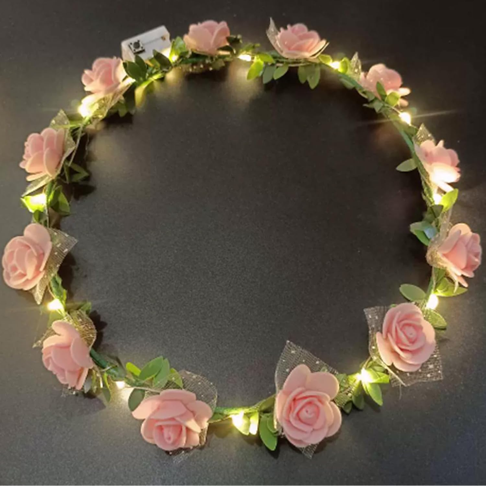Rosenkranz mit rosa Blüten und hellen Lichtern auf dunklem Hintergrund. Die Blumen und Blätter verleihen eine romantische Stimmung.