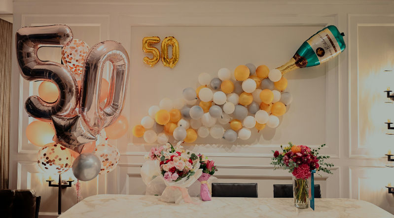 Geburtstagsdeko zum 50.: große 50-Luftballons, Champagnerflasche aus Ballons, Blumen und Tisch in heller Feieratmosphäre.