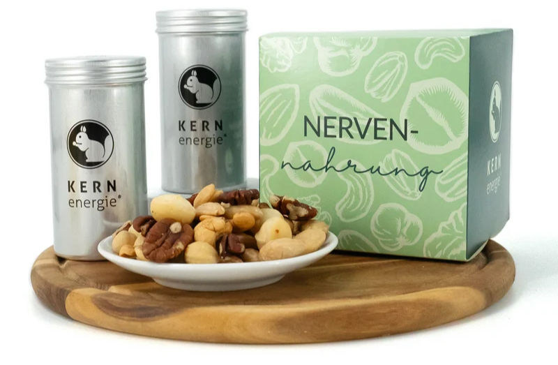 Silberdosen von KERN energie, Schale mit Nüssen auf Holzbrett und grüne Box mit Aufdruck NERVEN-nahrung.