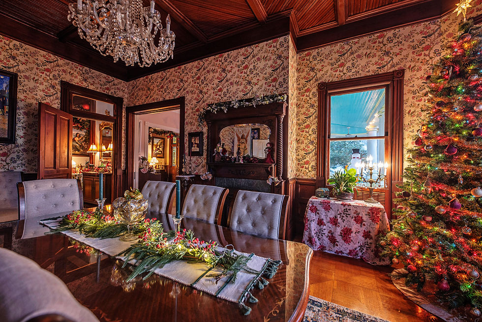 Elegant dining room with chandelier, floral wallpaper, holiday table decor, and a lit Christmas tree. Candles and lamps illuminate the space.