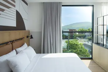 Guest room at Caption by Hyatt Chattanooga featuring custom mural wallcovering and two-tone painted walls by Dream Team Finishes, with floor-to-ceiling windows overlooking Lookout Mountain and the Southside neighborhood.