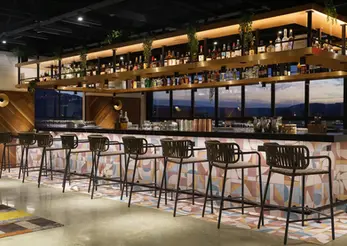 Indoor Stratus rooftop bar at Caption by Hyatt Chattanooga featuring polished concrete floors, geometric patterned tile, warm wood shelving, and painted surfaces finished by Dream Team Finishes, with mountain views through panoramic windows.