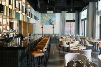 Nomia restaurant dining room at Caption by Hyatt Chattanooga featuring painted white brick walls finished by Dream Team Finishes, teal banquette seating, and floor-to-ceiling windows with natural light.