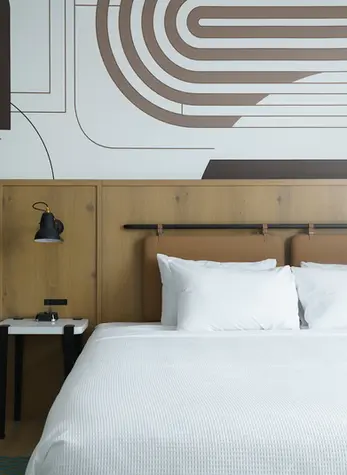 Close-up of a custom geometric arc mural wallcovering installed by Dream Team Finishes in a guest room at Caption by Hyatt Chattanooga, with painted two-tone walls above a leather and wood headboard.