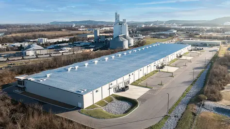 Aerial view of a large commercial building with a gray roof, surrounded by an industrial area, representing the type of properties serviced by Dream Team Finishes for painting and restoration.