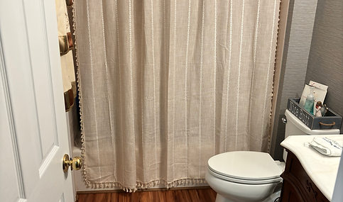 Bathroom with shower curtain, toilet, and hardwood floor. Renovations & Flooring.