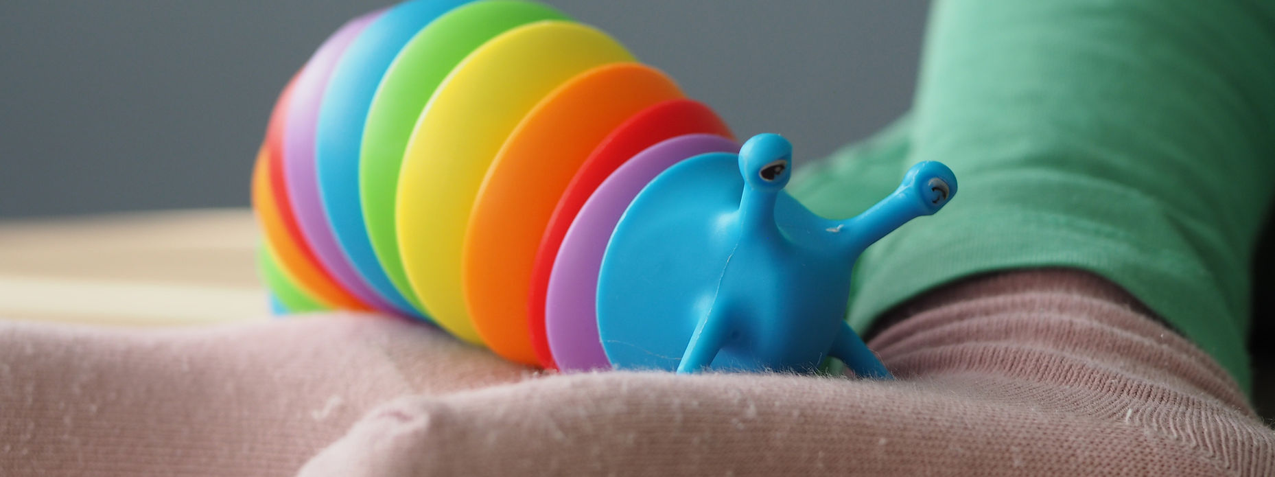 Eine regenbogenfarbene Fidget Toy Schnecke kriecht über den Fuß eines kleinen Kindes