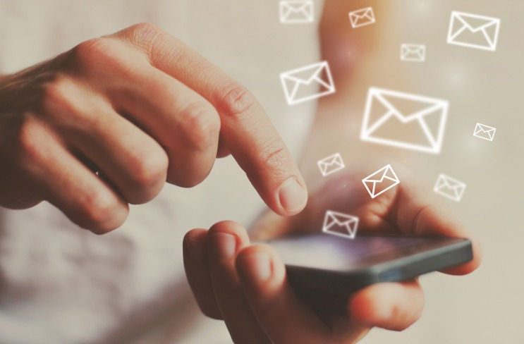 Non-descript hands holding a cell phone with images of email icons floating away.