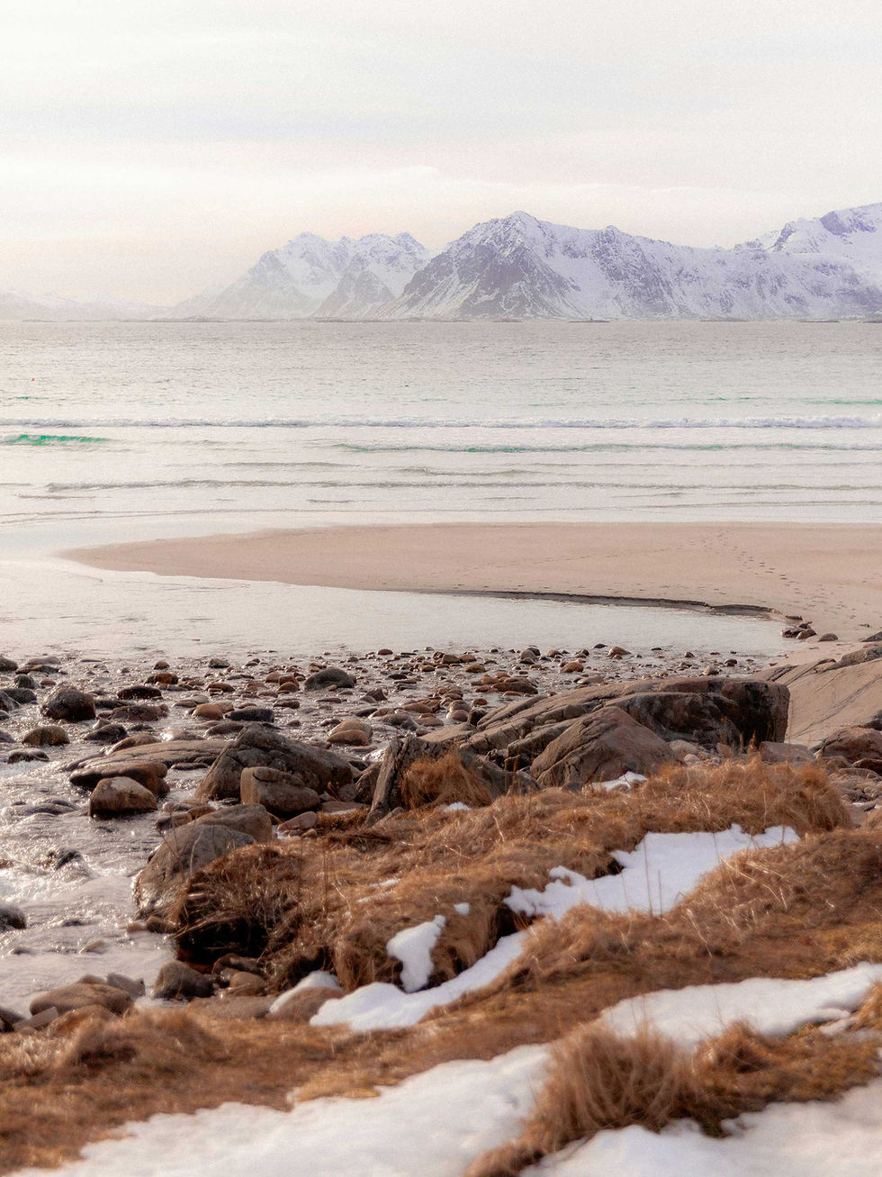 Snow-covered beach overlooking the sea and mountains of Norway.