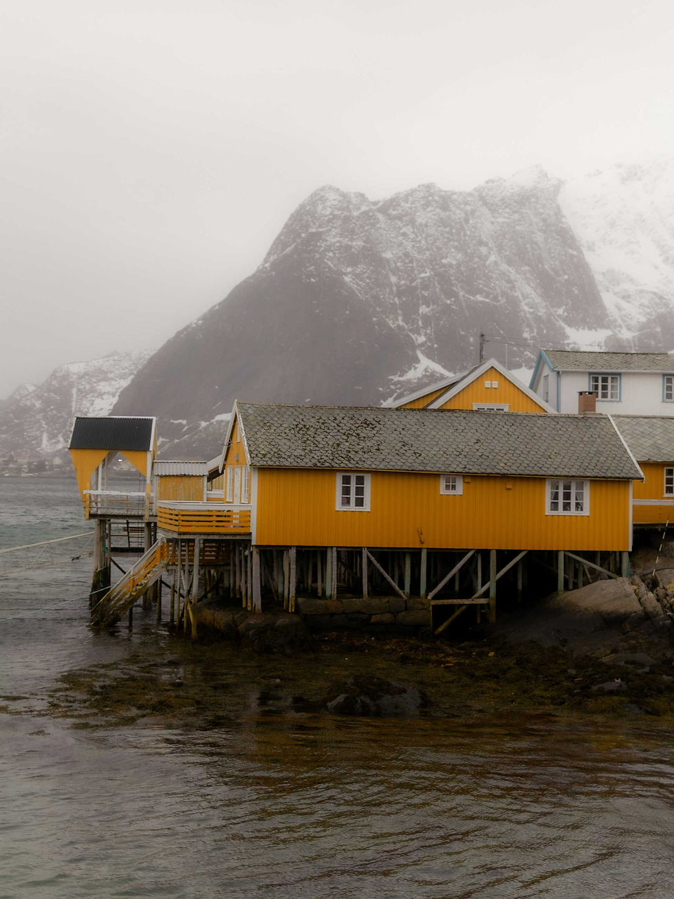 Traditional yellow fishing cabin on the waterfront beneath snow-covered mountains in Norway, Tromsø.
