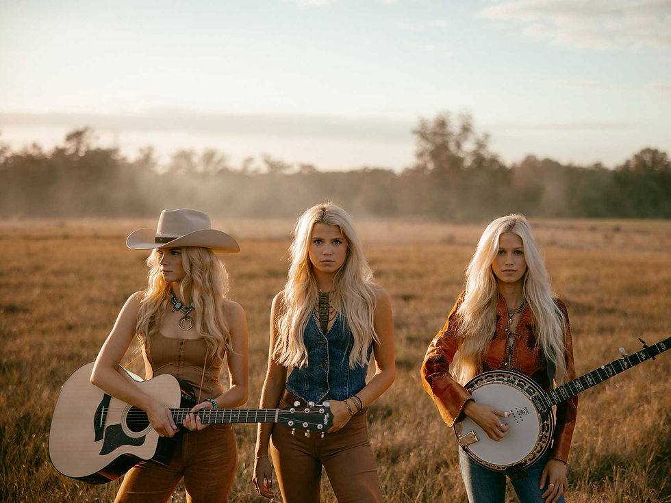 The Castellows sisters standing in a sunlit field with guitar and banjo, reflecting their neo-traditional country sound