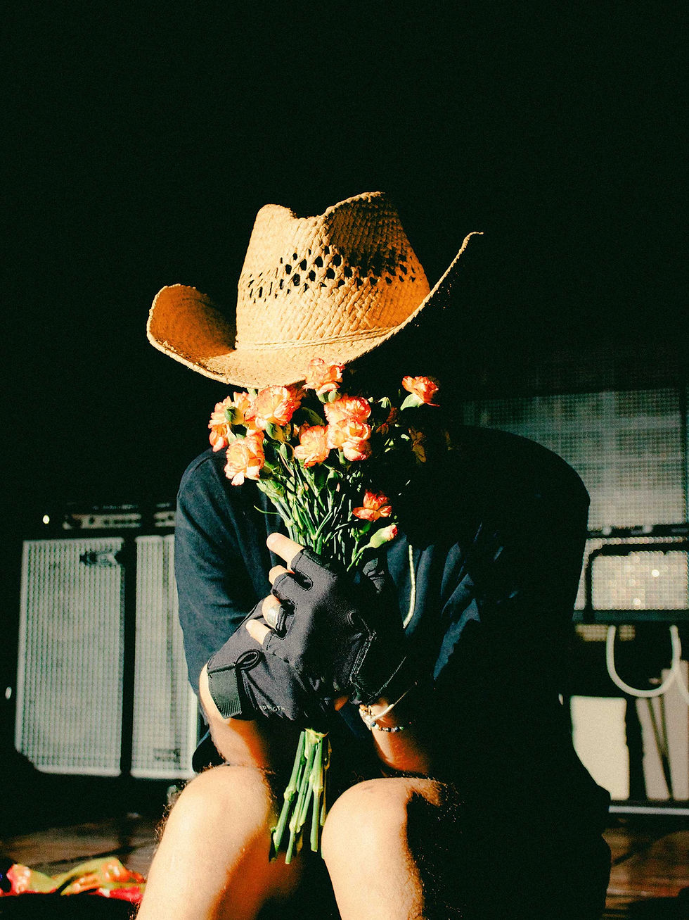 Person wearing a cowboy hat holding flowers in front of their face at a country music event