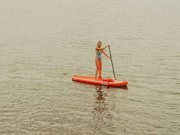 Woman paddle boarding on calm open water on a bright red stand-up paddle board.