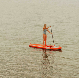 Woman paddle boarding on calm open water on a bright red stand-up paddle board.