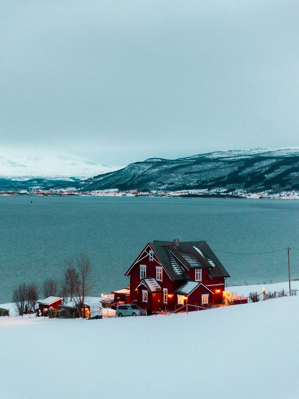 Traditional red Norwegian house beside a fjord in the snow-covered Tromsø, Norway.
