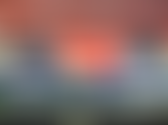 Two men seated at a table with "Narasumber" and "Moderator" nameplates, engaged in discussion. A blue cloth and floral arrangement adorn the table.