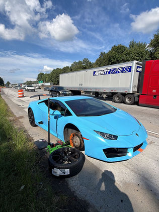 Light blue Lamborghini sports car with front wheel removed during roadside tire service.