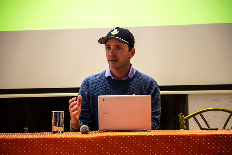 A man in a baseball cap speaking behind a laptop at a panel.