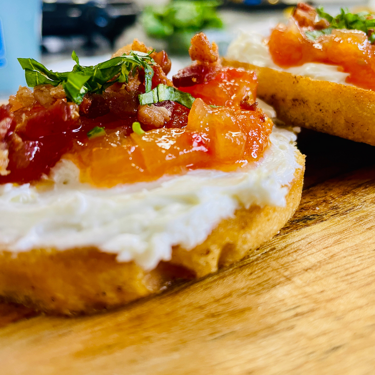 Close-up appetizer on toasted bread with creamy spread, orange-red jam, and herbs