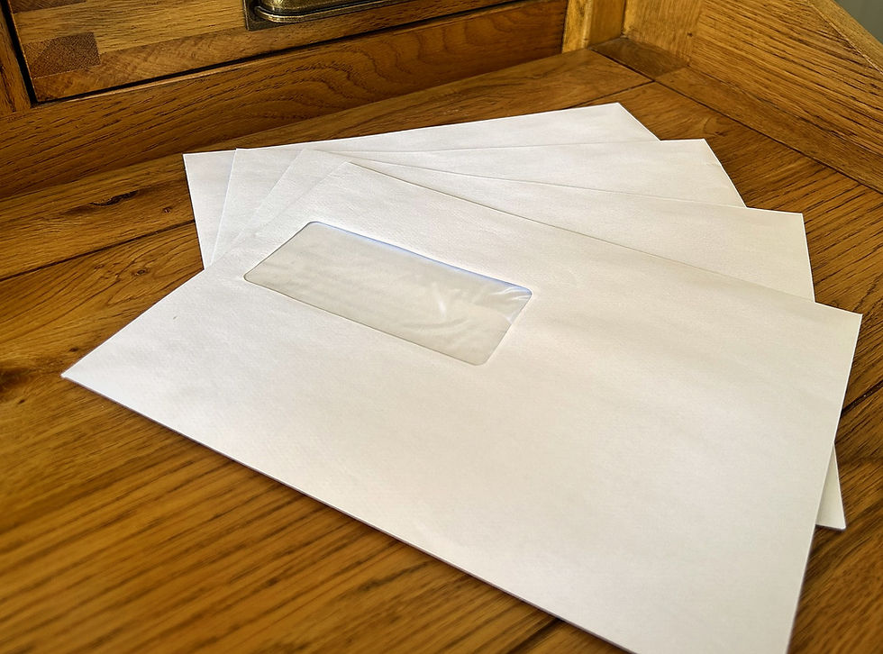 Several unopened white envelopes with address windows, fanned out on a wooden desk, representing the wait for A-level results