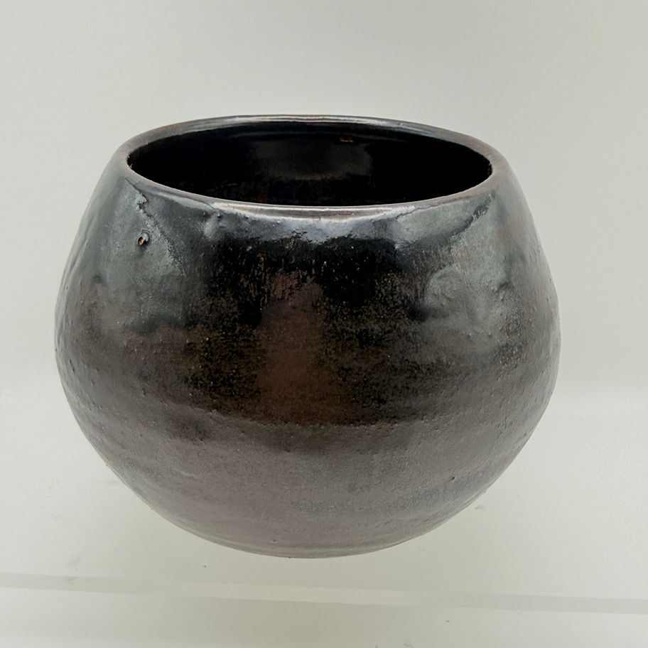 Handmade round ceramic bowl with a glossy dark metallic glaze on a white background.