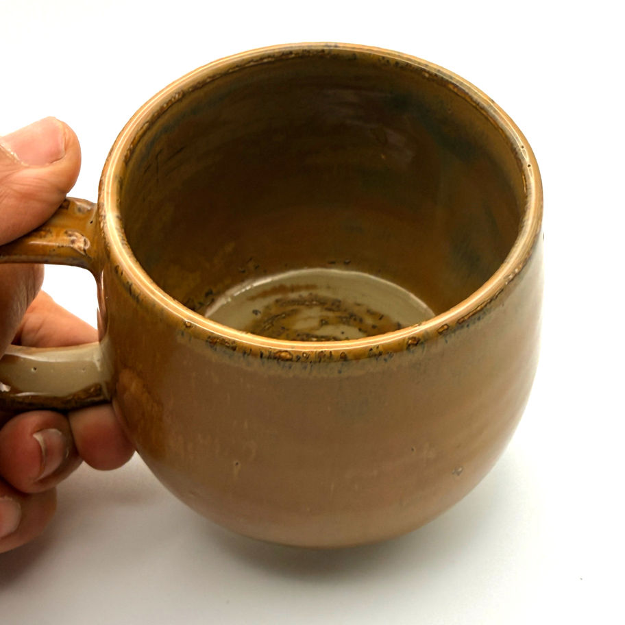 A handcrafted brown ceramic mug with glossy ochre glaze arranged on a white surface.