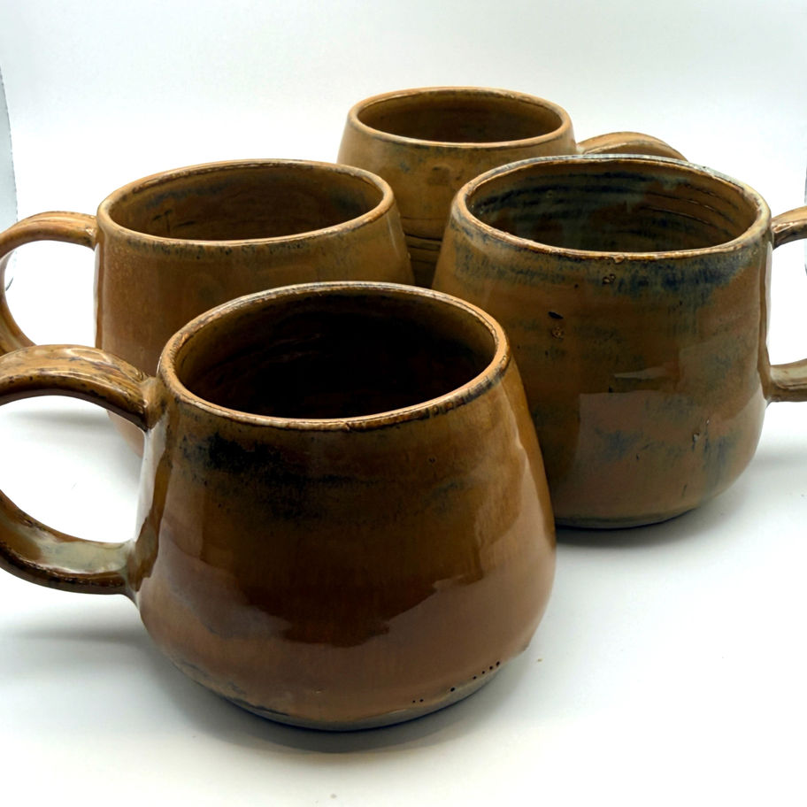 Four handcrafted brown ceramic mugs with glossy ochre glaze arranged on a white surface.
