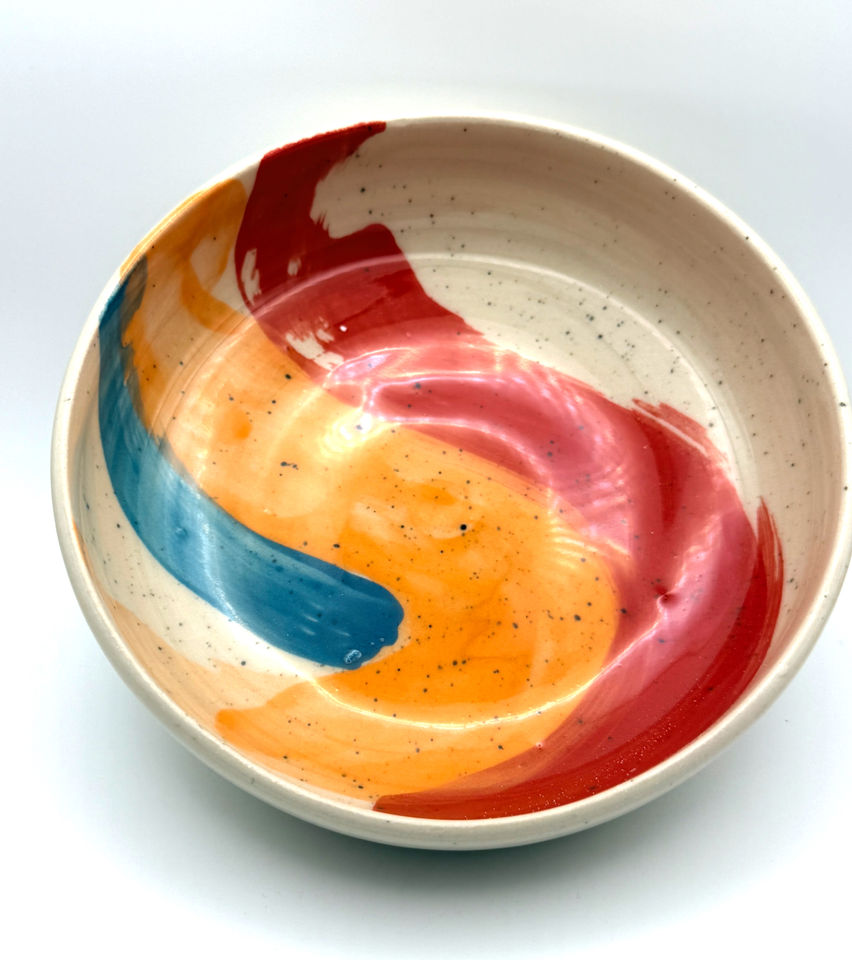Handcrafted speckled ceramic bowl with abstract red, orange, and blue brushstrokes.