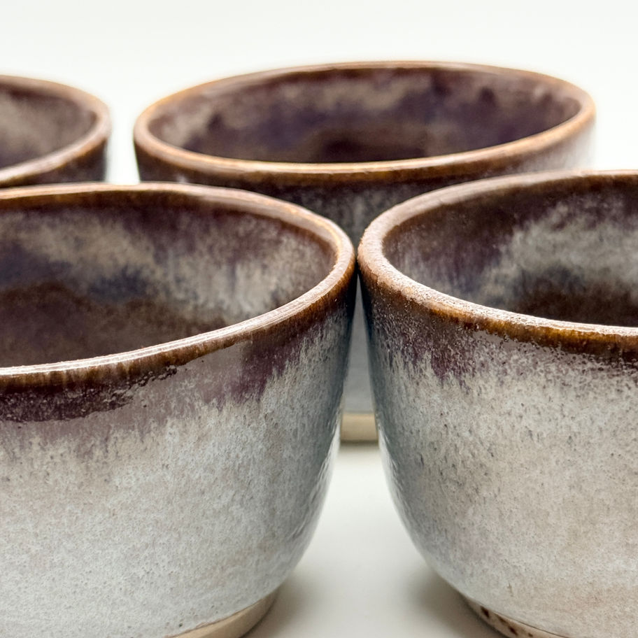 Set of four handmade ceramic tea bowls with a speckled purple and light grey glaze on a white background.