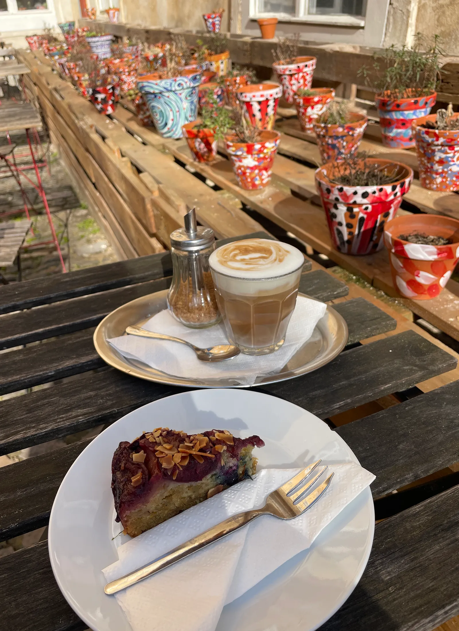 Kafe & Hrnky kohviku sisehoovis on laual cafe latte ja tükk kooki