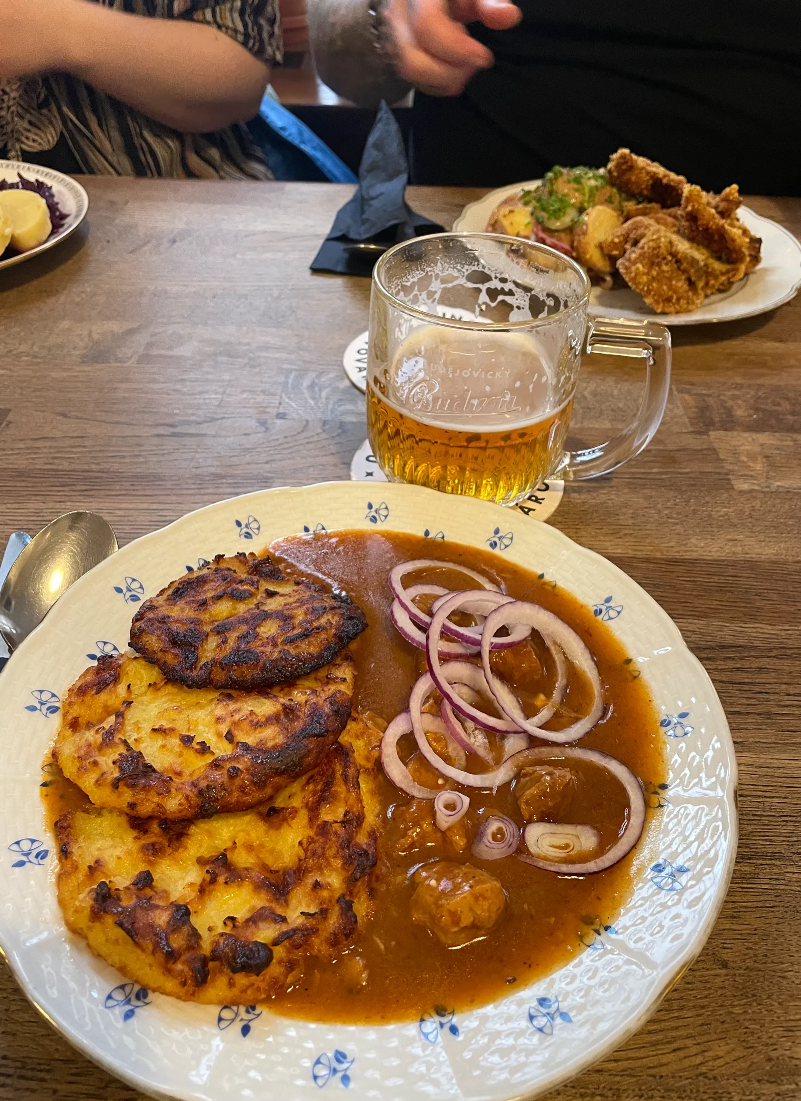 Restoran Střechas taldrik kartulipannkookide ja guljašilaadse kastmega, peal punase sibula viilud, kõrval kann õllega