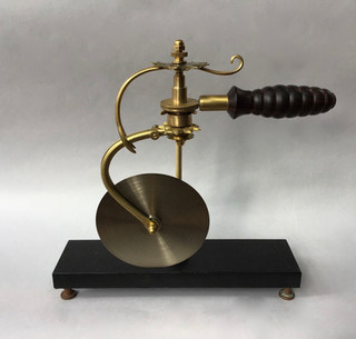 Handmade pizza cutter: turned cocobolo handle fixed to ornate swivel-caster frame with 5 inch rotary blade. Acrylic and brass stand. 1877