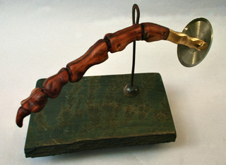 Handmade pizza cutter: manzanita wood handle carved as life size replica of cretaceous bird-like dinosaur claw. Slate stand. 1892