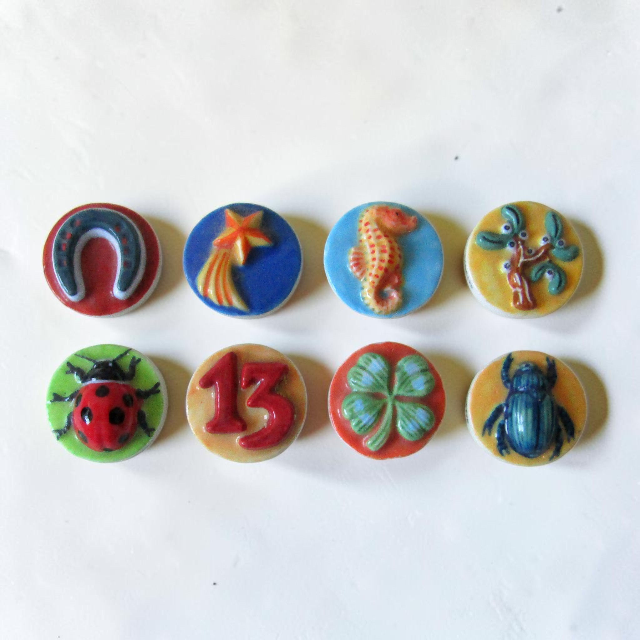 Fèves en porcelaine brillante Porte-Bonheur 1 (Éditions Prime, 2004), série de 8 médaillons colorés représentant des symboles