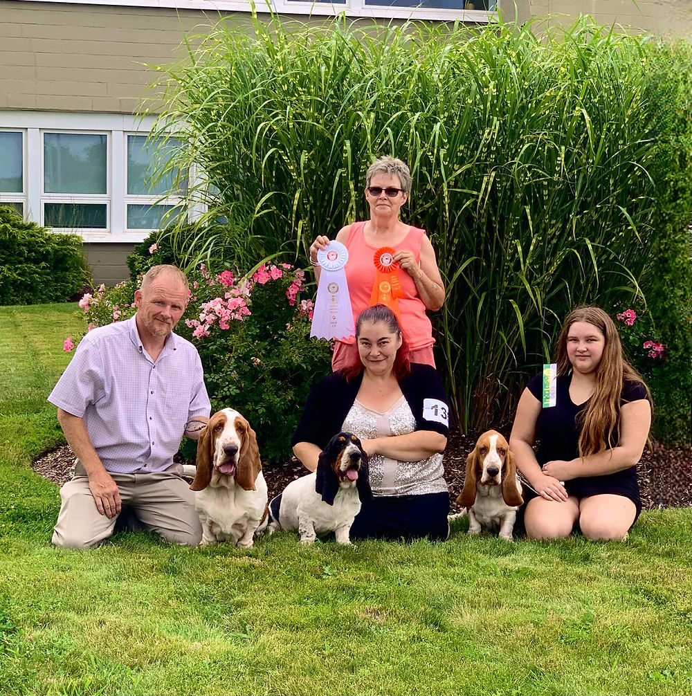basset hounds and people posing in a group with win ribbons