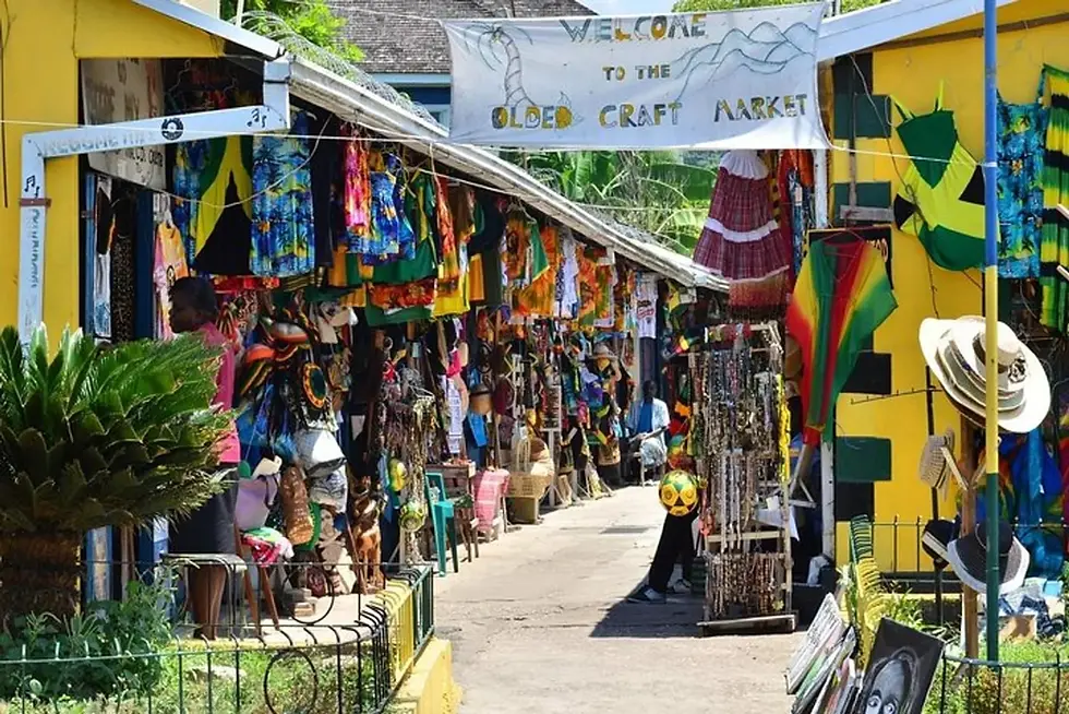 Outdoor Jamaican craft market walkway with colorful stalls and a Welcome to the Olde Craft Market banner.