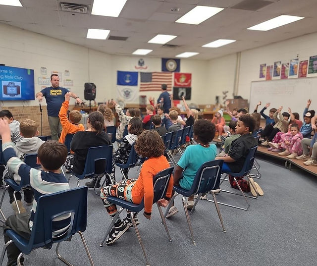 A leader addresses a large group of elementary-aged children in an after school Bible club