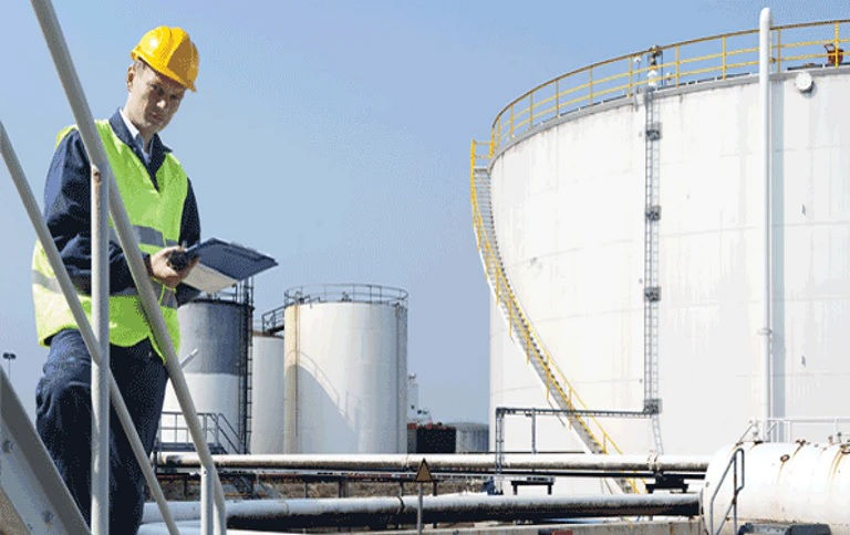 Man with yellow helmet standing on top of storage tanks