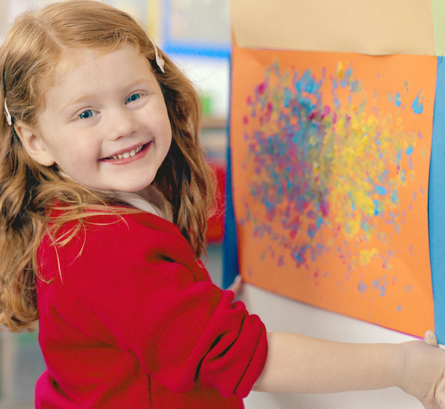 Smiling child in red sweater shows colorful abstract painting on orange paper. Bright background with a joyful mood.