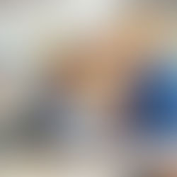 Young boy in a classroom receiving a paper from a teacher. He looks curious. Background shows desks and shelves with books.