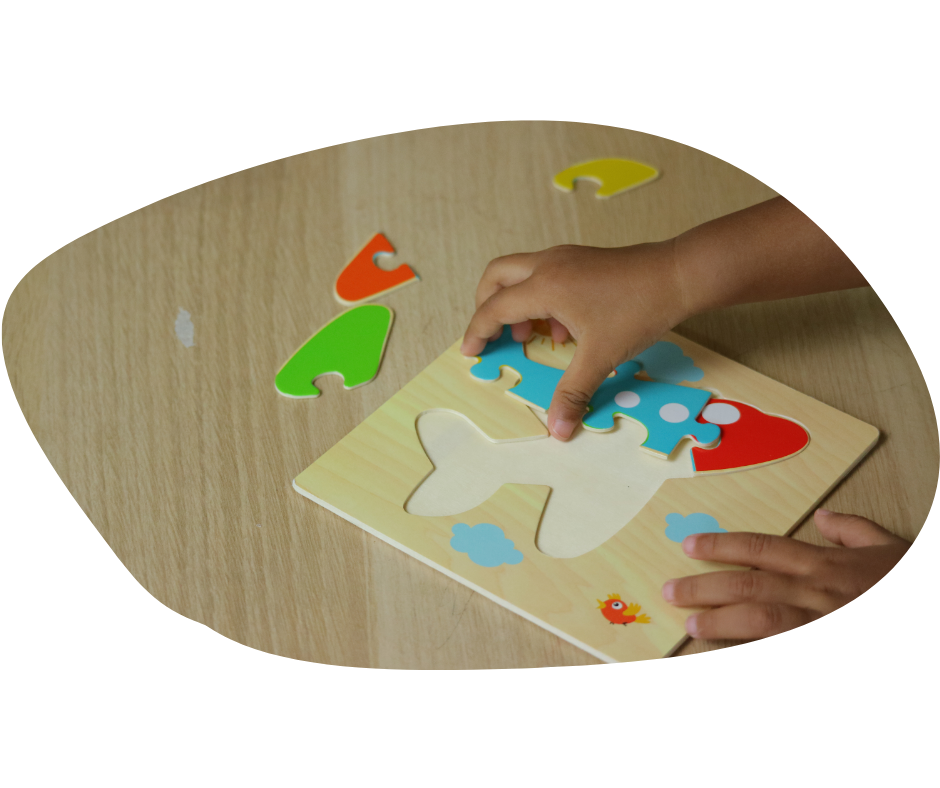 Child assembling colorful airplane puzzle on wood table. Puzzle pieces are red, blue, green, and yellow, creating a playful mood.